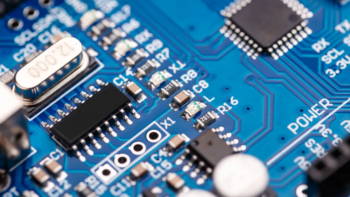 Close-up of a blue circuit board with a crystal oscillator, SMD components and a microcontroller, bright industrial photography